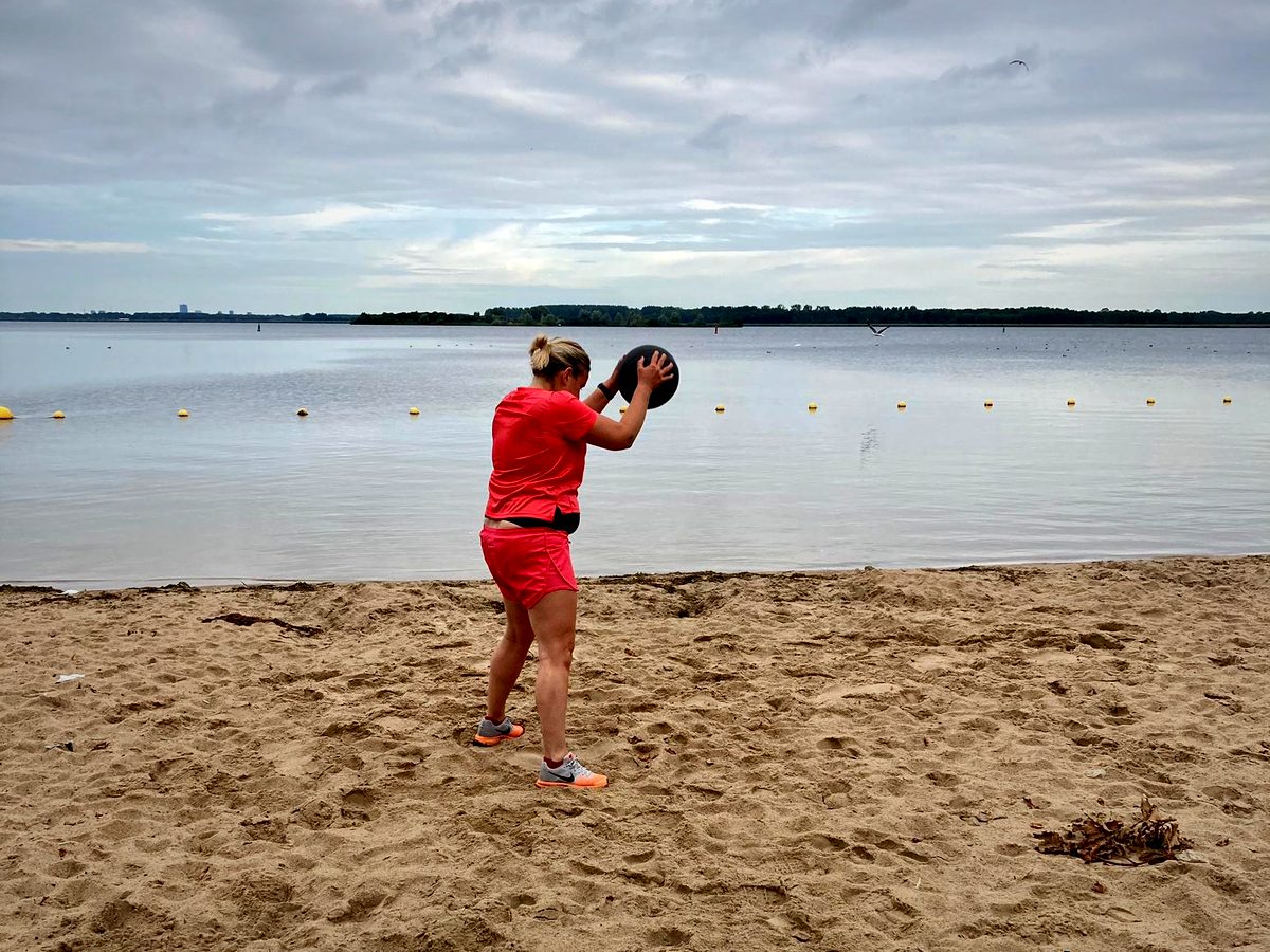 Iemand houdt een medicinebal boven het hoofd op het strand