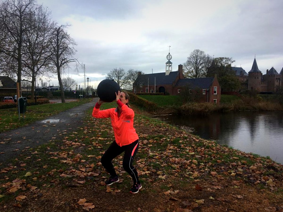 Iemand werpt een medicinebal omhoog op een pad langs het water