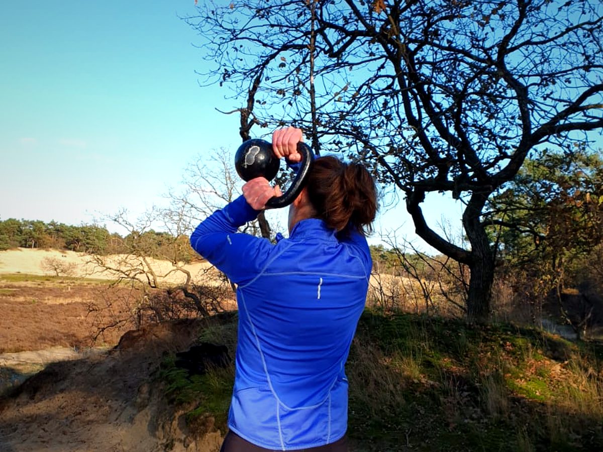 Iemand houdt een kettlebell boven het hoofd buiten bij bomen