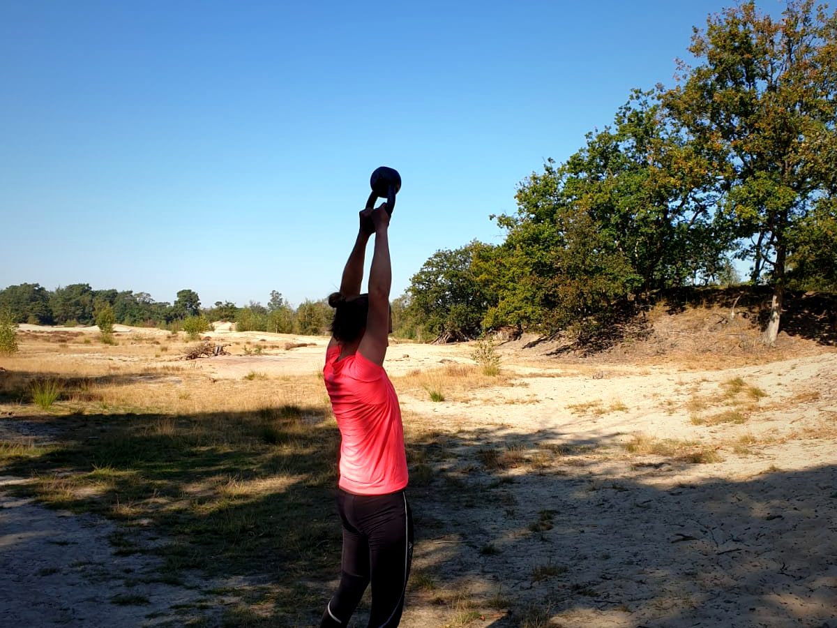 Iemand strekt een kettlebell boven het hoofd in de duinen
