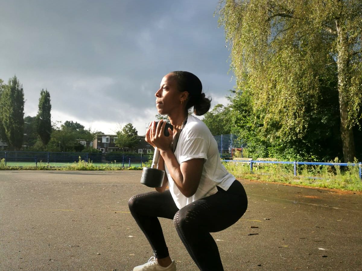 Iemand zakt diep door de knieën met een kettlebell op een grijze dag